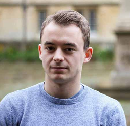 Portrait of a young man in a blue sweater outdoors with a blurred building background