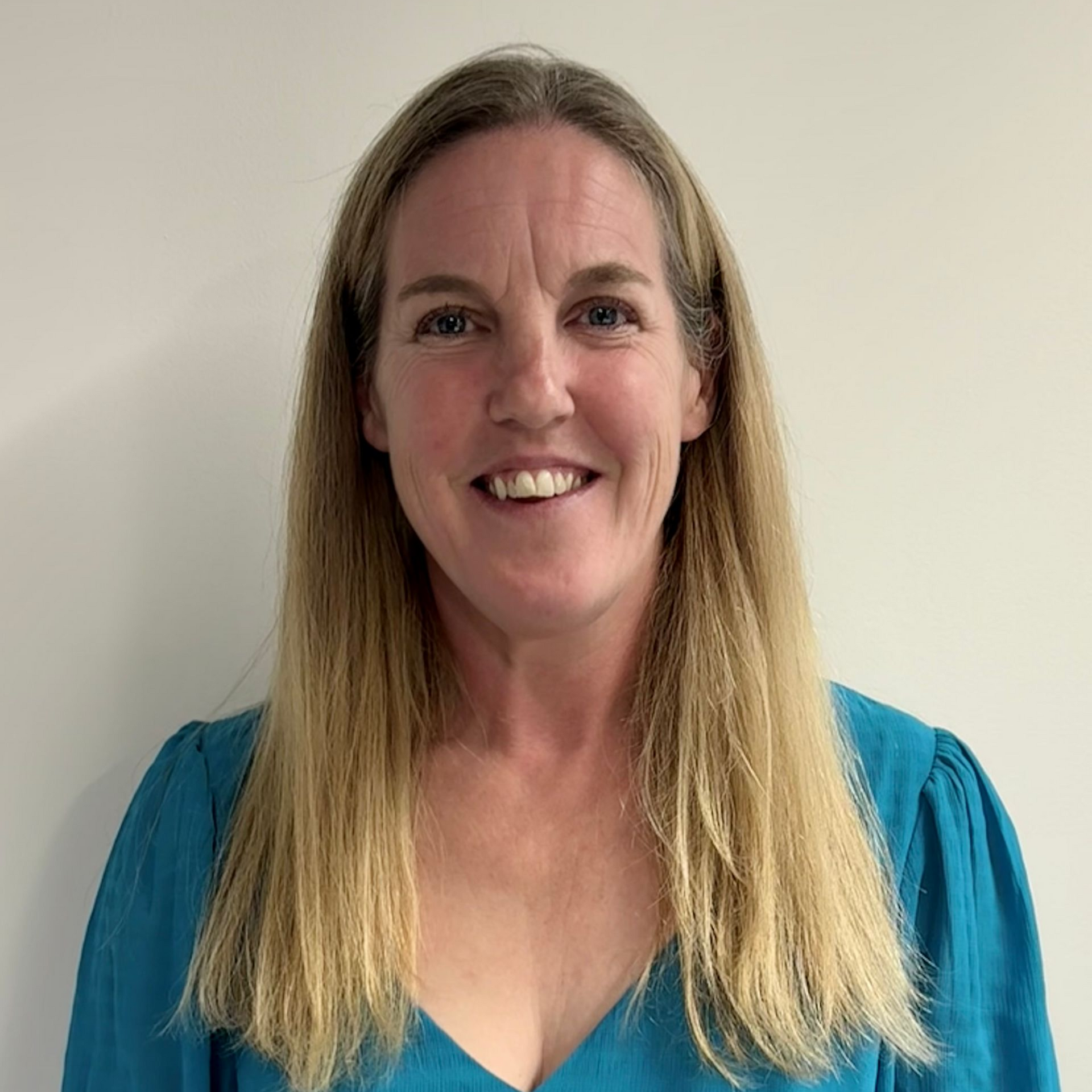 Portrait of a smiling woman in a teal top against a plain wall