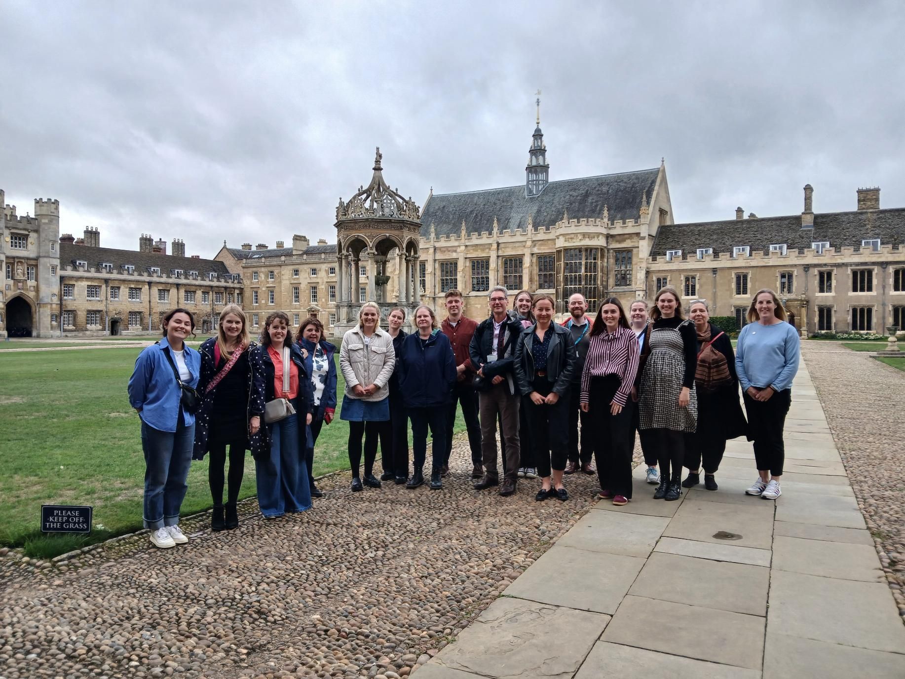 Group posing in a courtyard before a historic stone building under a cloudy sky
