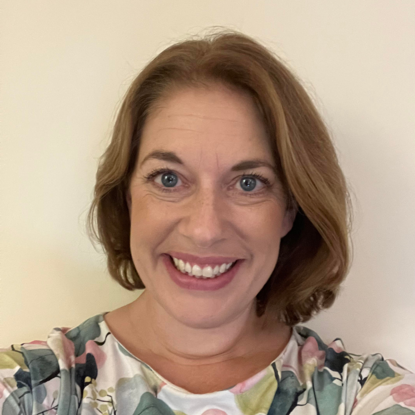 Smiling woman in a floral top against a plain wall