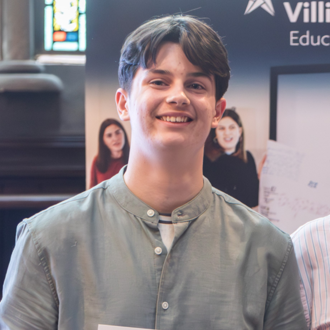 Smiling person in a gray shirt standing indoors at an event booth