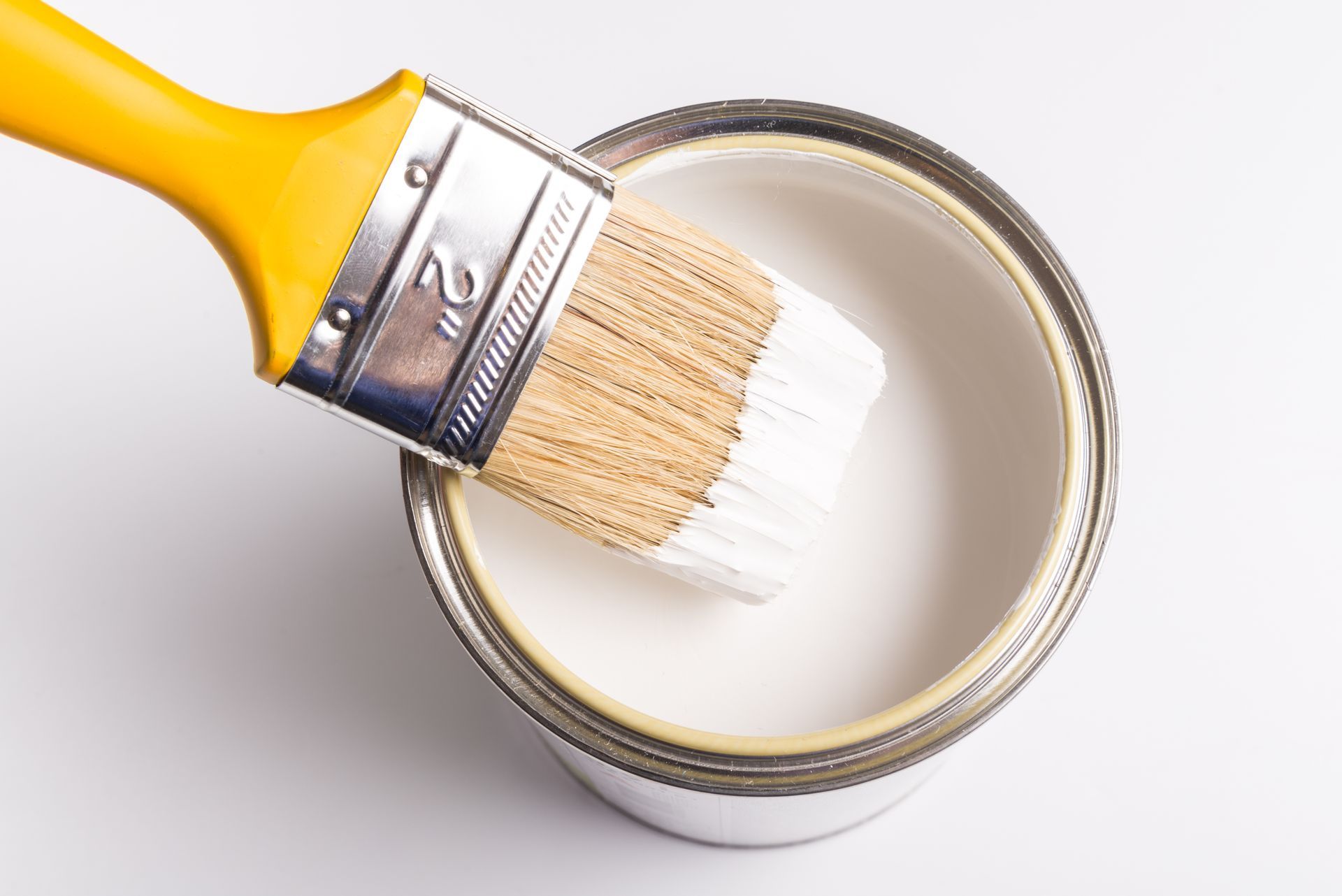 A brush is dipping into a can of yellow paint.