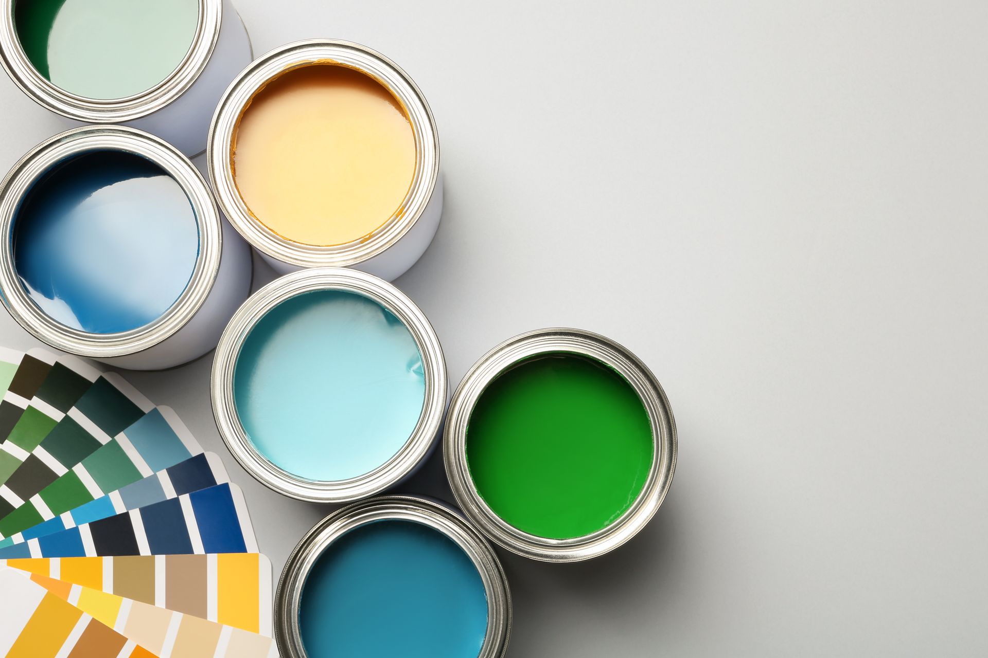 Open paint cans in various colors with a color swatch fan on a gray surface.
