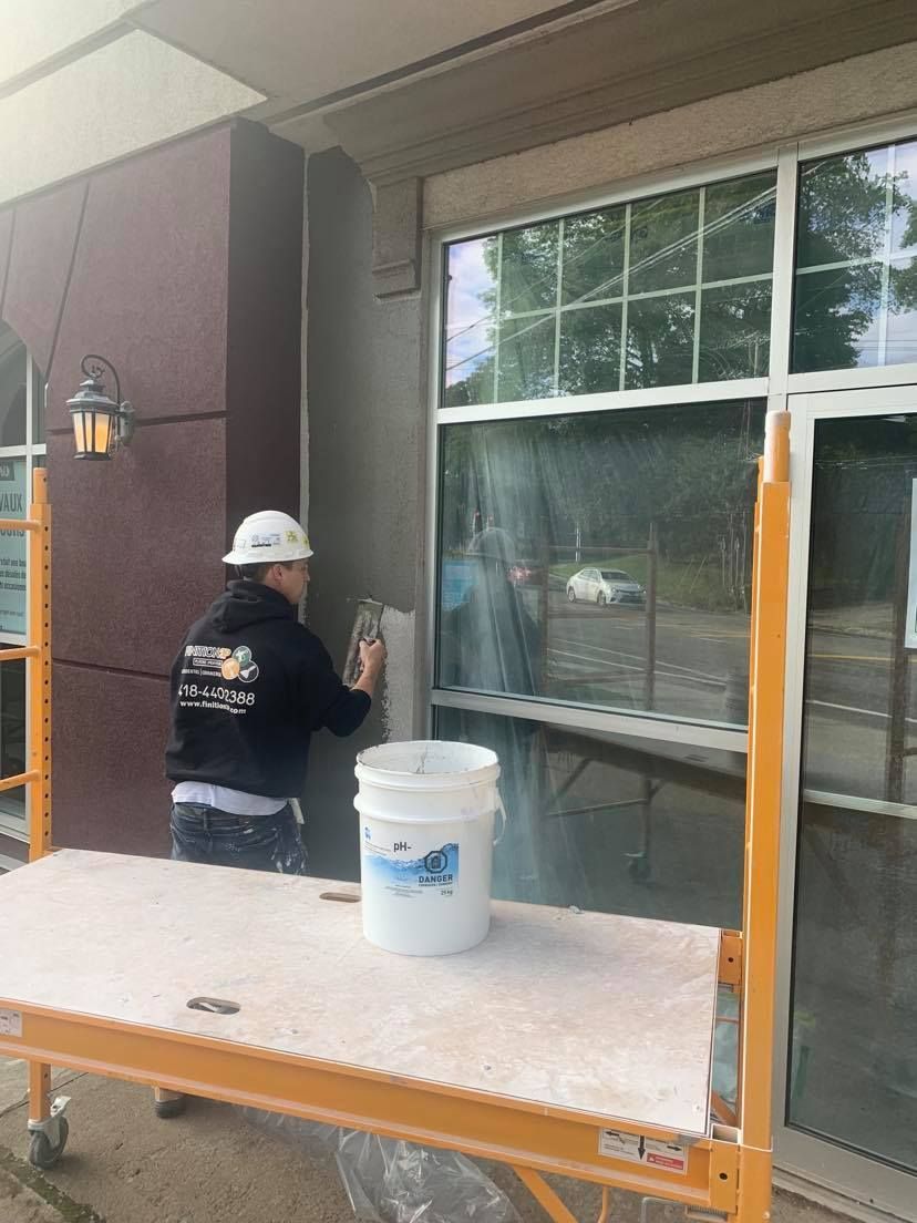 A man is standing on a ladder painting the side of a house.