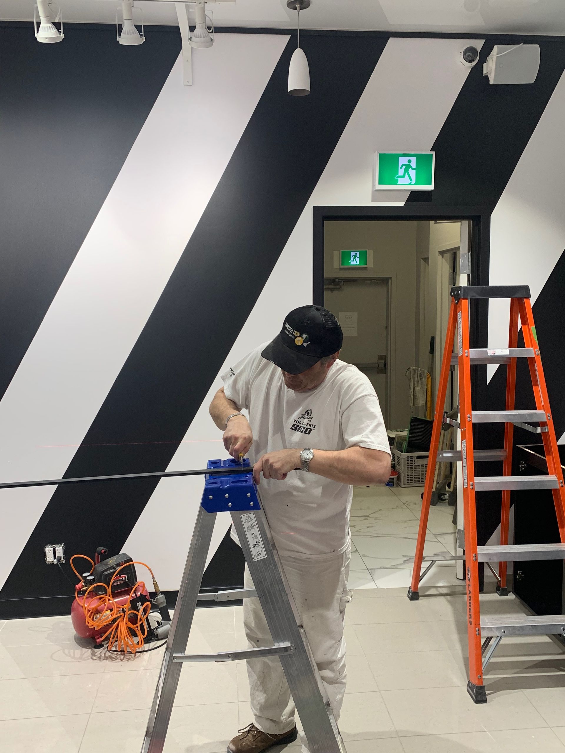 A man is standing on a ladder in front of a black and white striped wall.
