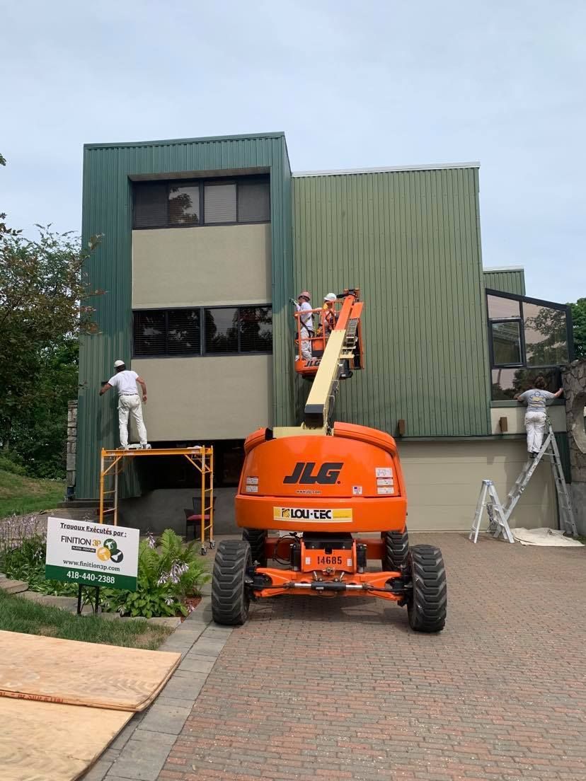 A large building is being painted with a jlg lift.