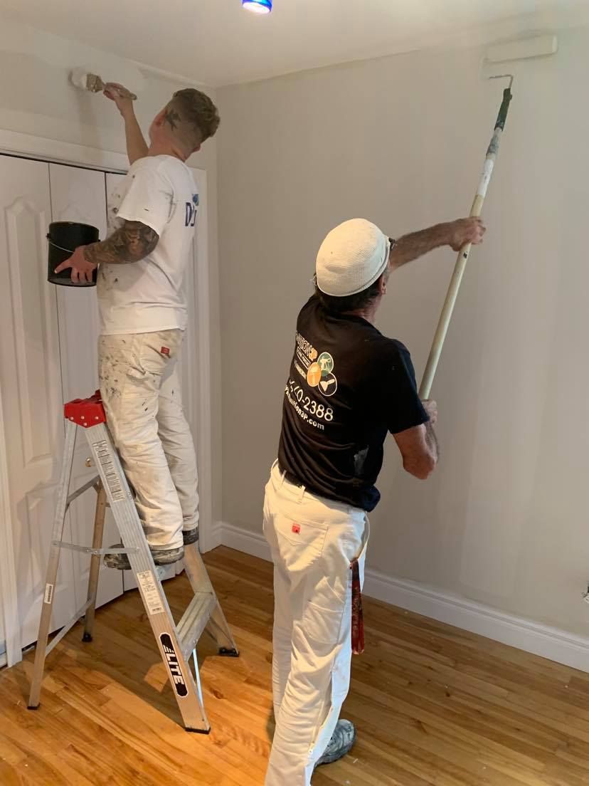 Two men are painting a wall in a room.