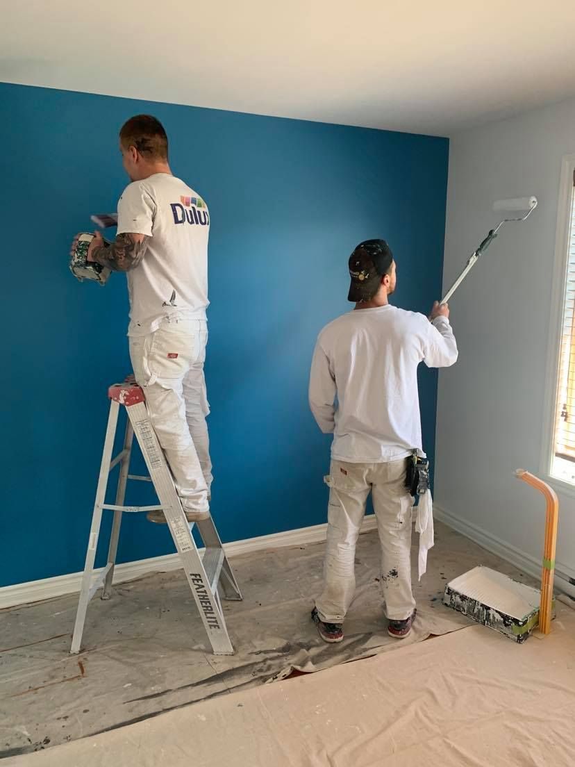 A man is standing on a ladder painting the side of a house.