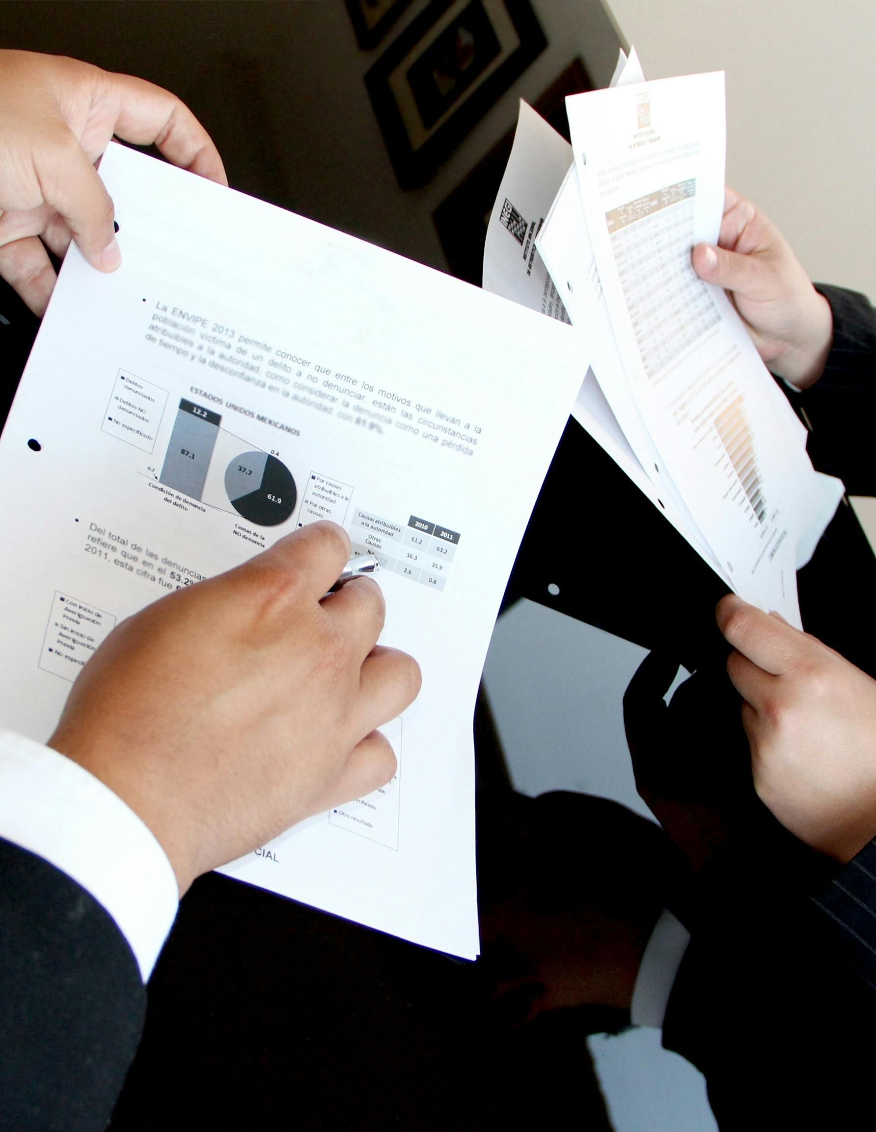 Two people in suits examining printed reports at a black table, charts visible.