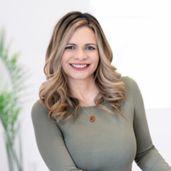 Smiling woman with wavy blonde hair in a sage top against a bright white background
