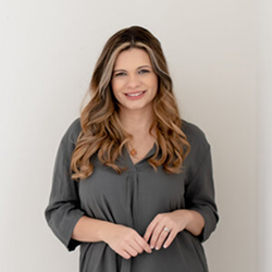 Smiling person in a dark gray top standing against a light background