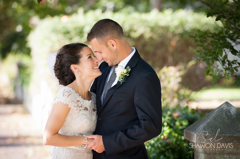 Bride and groom embrace outdoors under soft sunlight, sharing a tender forehead touch.