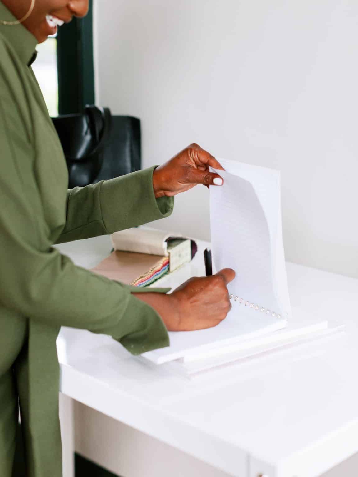 Person placing paper into a white ballot box on a desk, with a pen and notebook nearby.