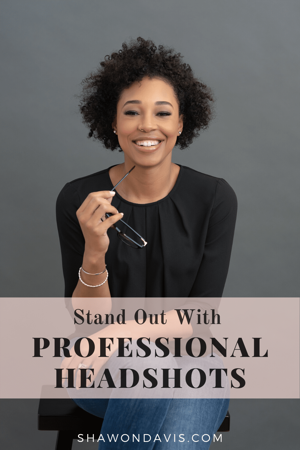 Smiling woman holding eyeglasses against a gray background with text: Stand Out With Professional Headshots