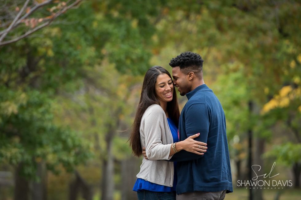 Couple embracing outdoors among green trees, smiling and holding each other closely