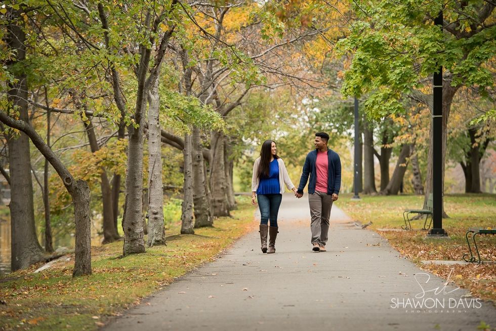 Two people walking hand in hand down a tree-lined park path in autumn