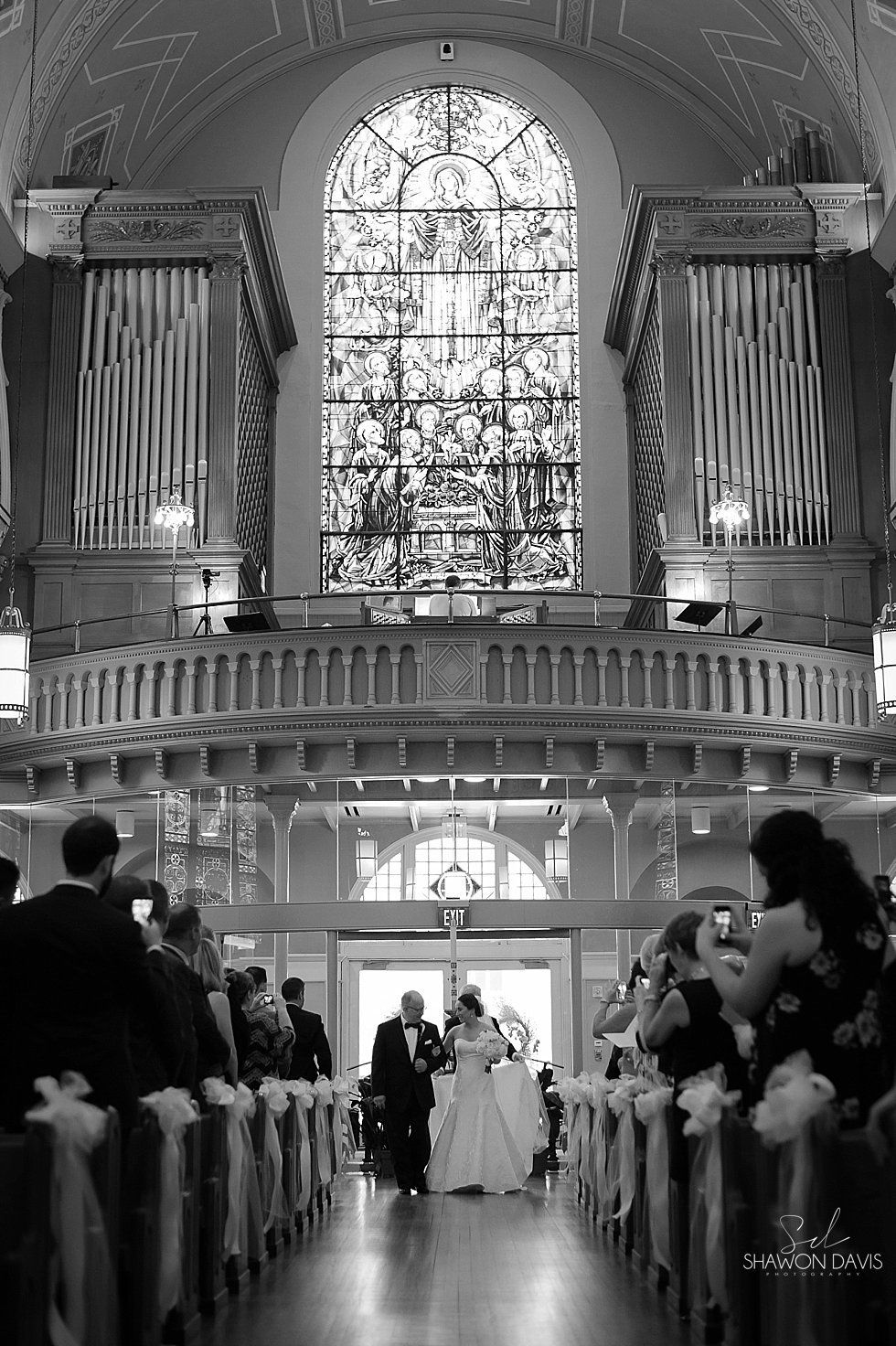 Wedding ceremony in a grand church aisle, with guests seated and the bride and groom at the altar.