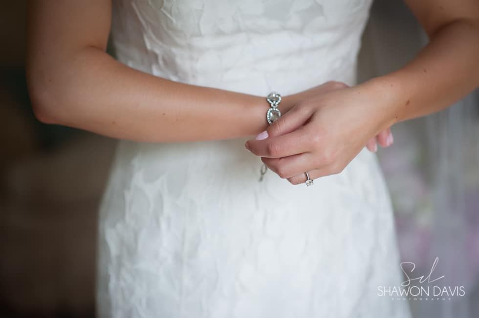 Bride in a white dress, hands clasped at her waist, with a silver bracelet visible.