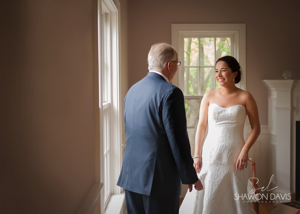 Bride in a white dress smiling at a man in a blue suit in a sunlit room