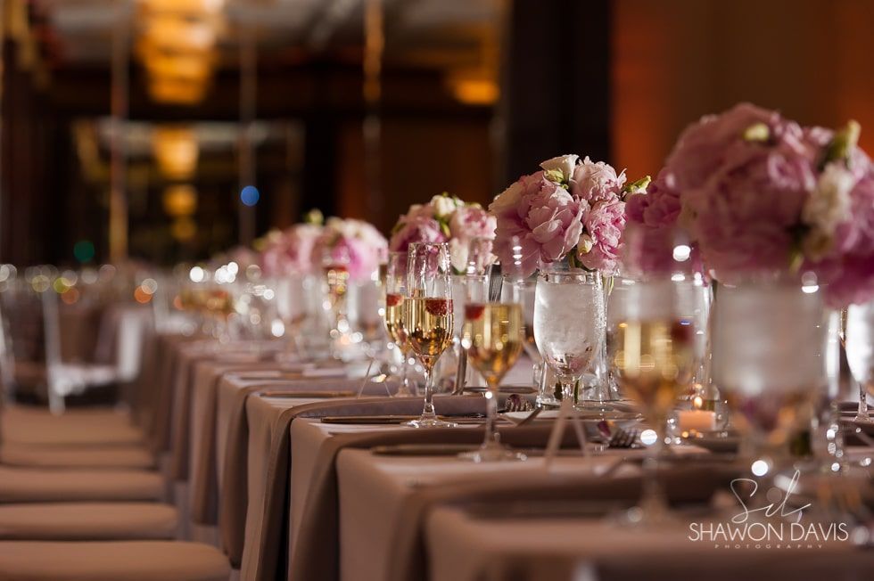Elegant banquet table with pink floral centerpieces and glassware in a warm, softly lit venue