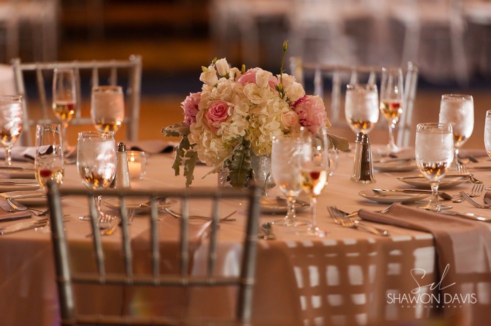 Elegant banquet table with floral centerpiece, candles, glassware, and gold accents in warm lighting