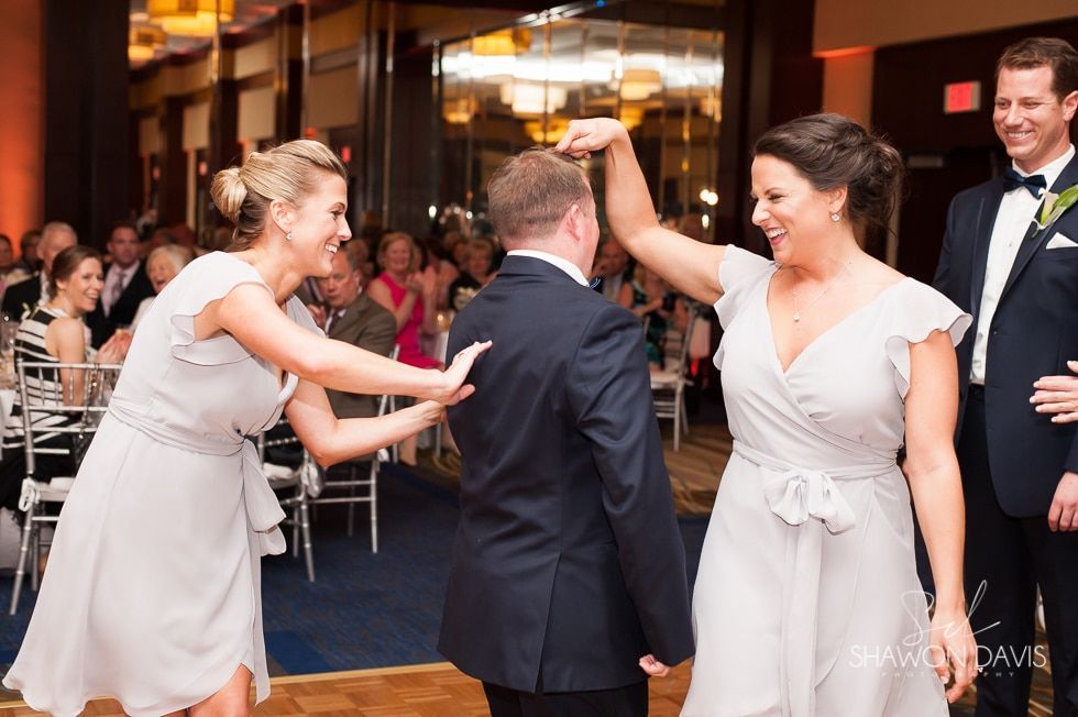 Wedding guests celebrate with high-fives on a dance floor in a warmly lit reception hall