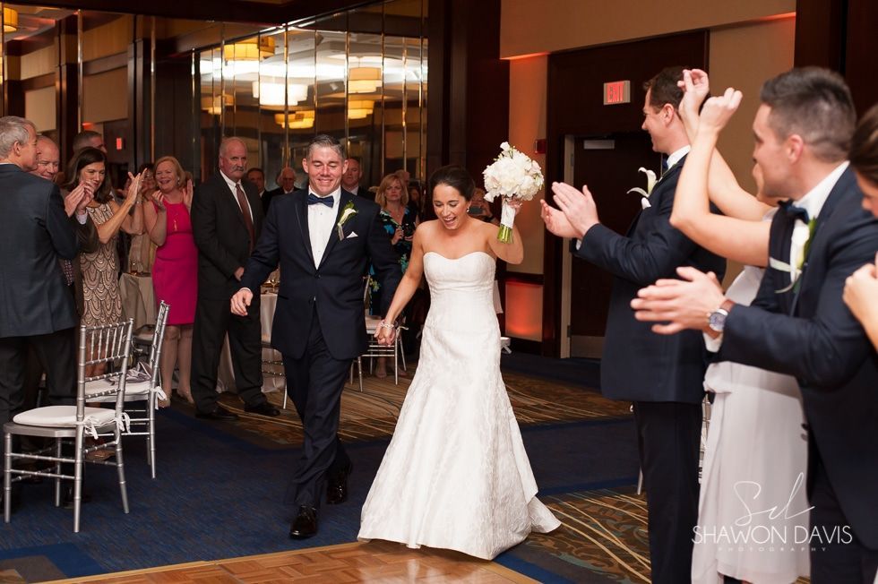 Bride and groom entering a reception hall, guests applauding on both sides
