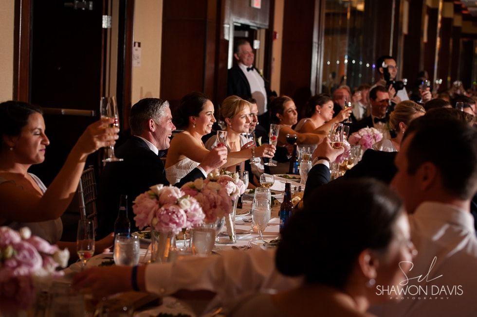 Guests toast at a candlelit banquet table with pink floral centerpieces in a formal reception hall