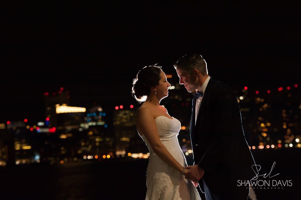 Bride and groom holding hands at night with city lights in the background