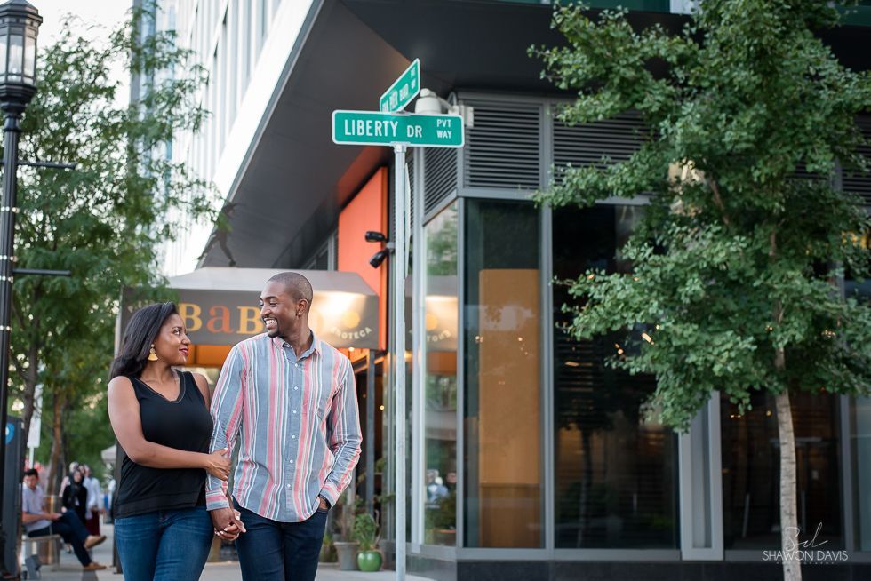 Two people talking on a city sidewalk by a Liberty street sign and glass storefronts.