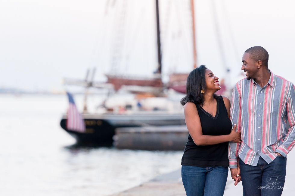 Two people smiling and talking by a marina with sailboats in the background