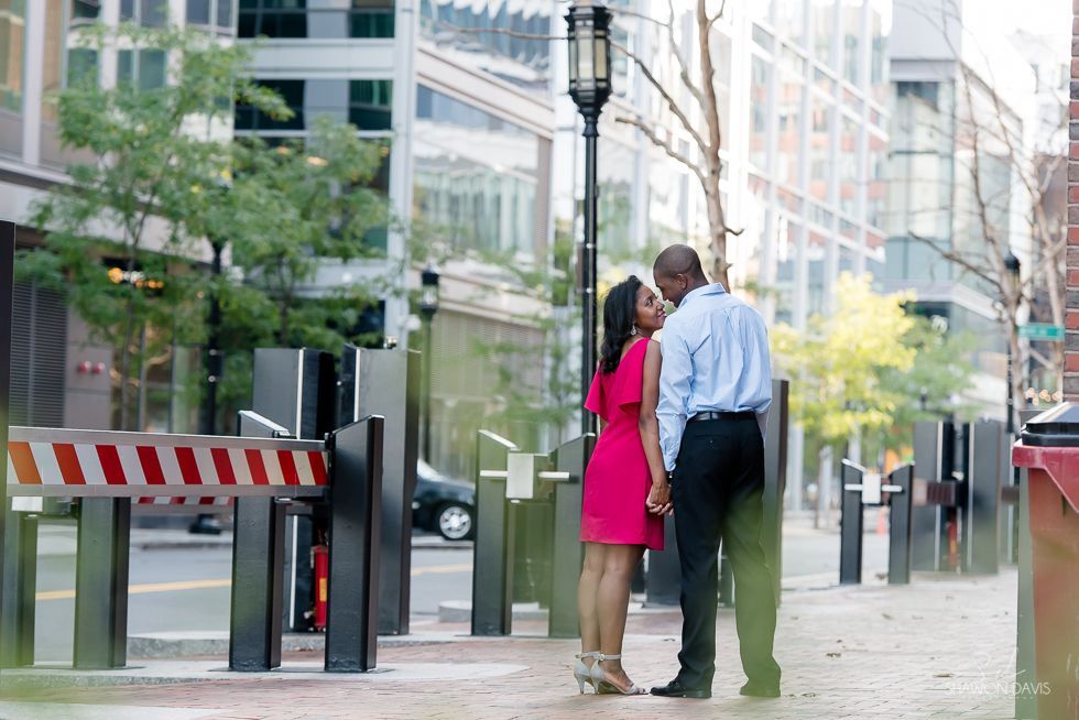 Two people standing by a gated entrance on a city sidewalk, talking beside a building.