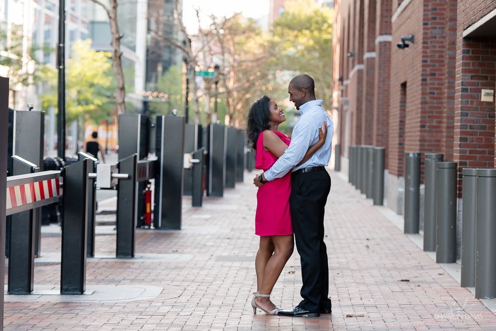 Couple embracing on a city sidewalk between brick buildings and bollards
