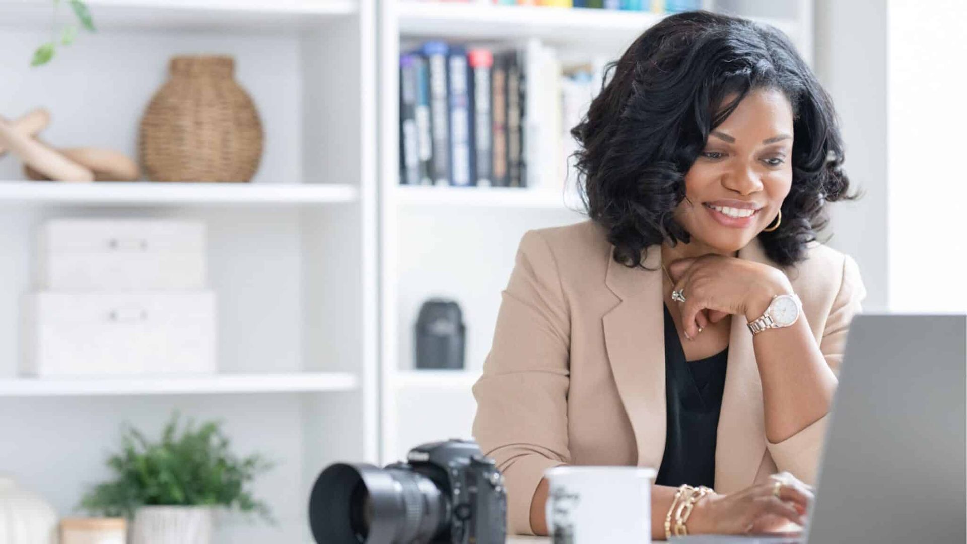Woman smiling at a desk with a camera and coffee cup in a bright office workspace