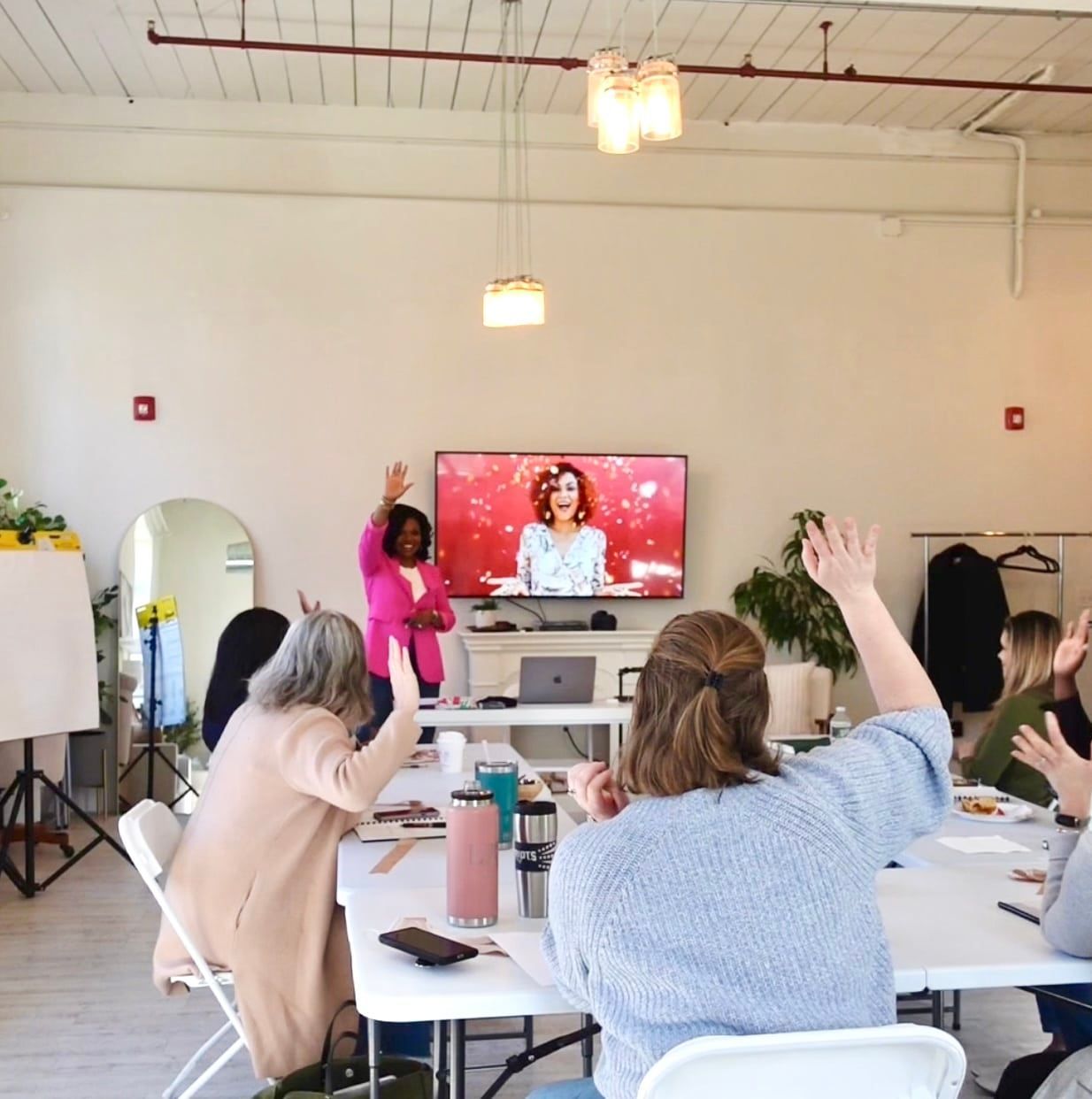 People seated in a meeting room watching a presentation on a TV screen, one person raising a hand.