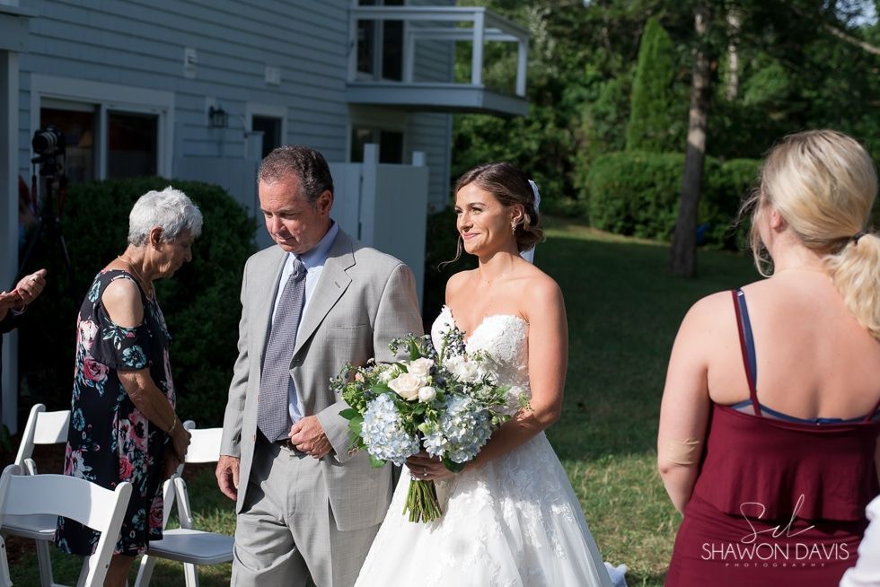 Bride holding bouquet walks with a man outdoors at a wedding ceremony