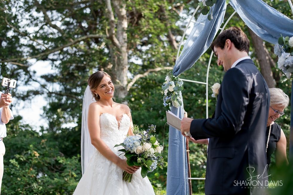 Bride and groom exchanging vows under a blue canopy in a garden ceremony