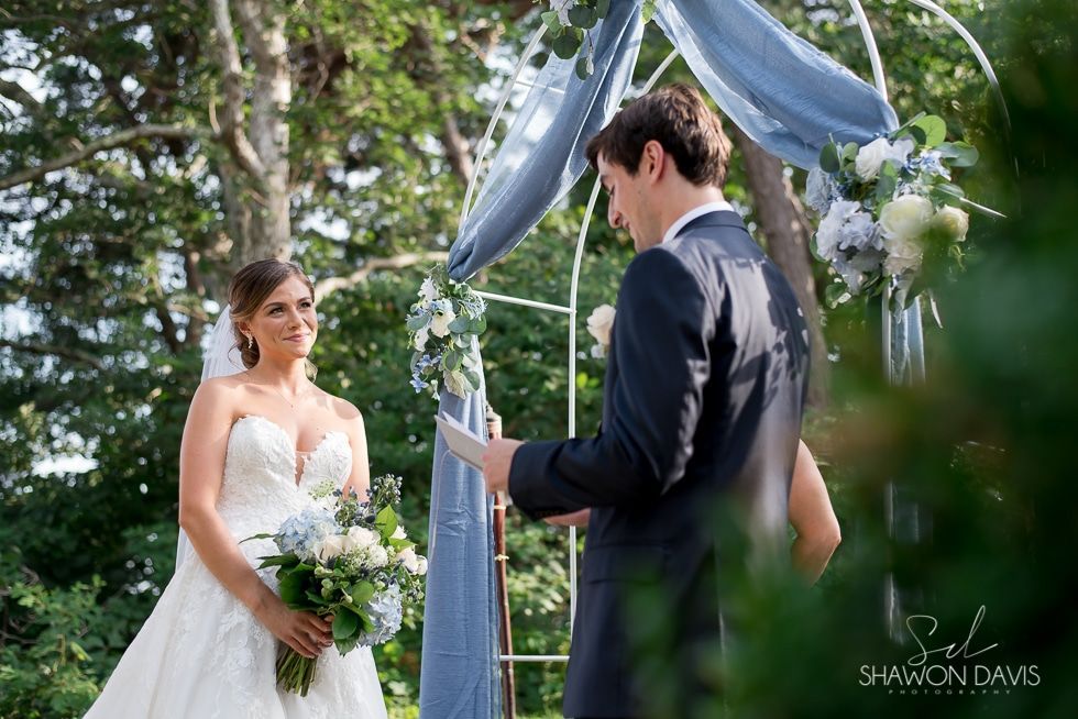 Bride and groom exchanging vows under a white floral arch outdoors