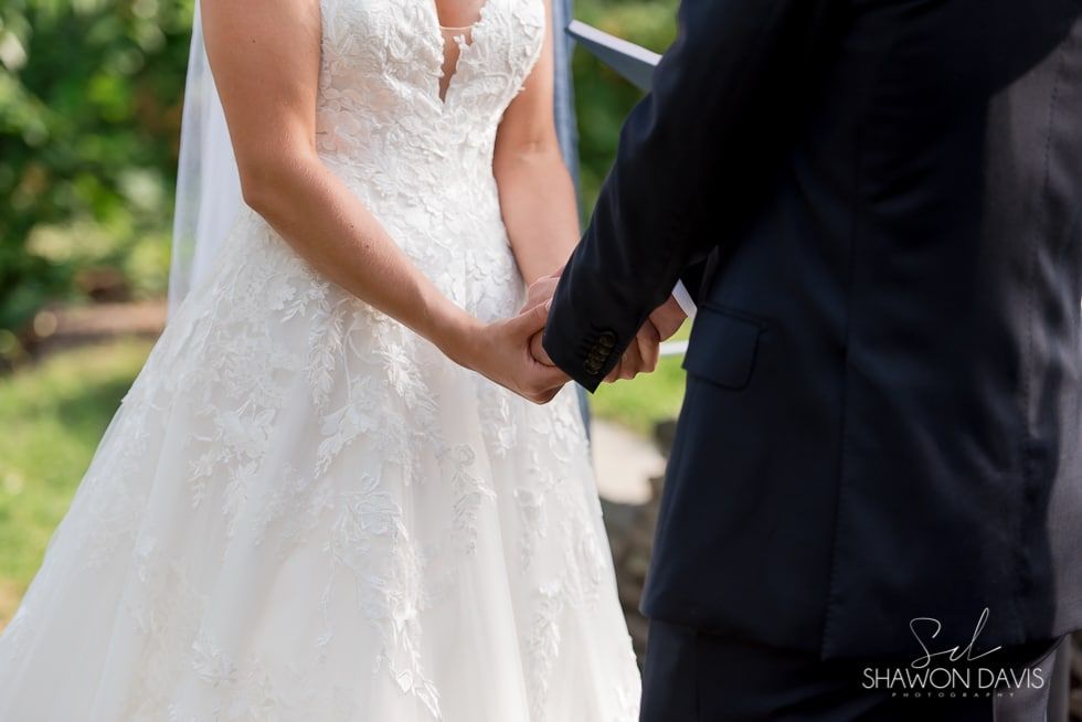 Bride in white wedding dress holding hands with groom in dark suit outdoors