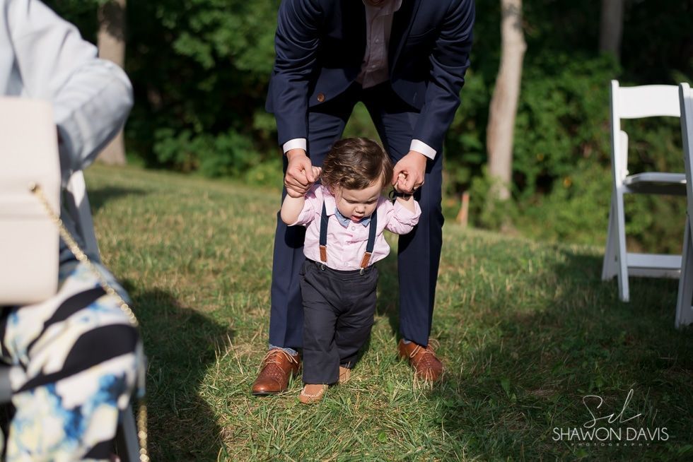 Adult helping toddler walk on grass at an outdoor event