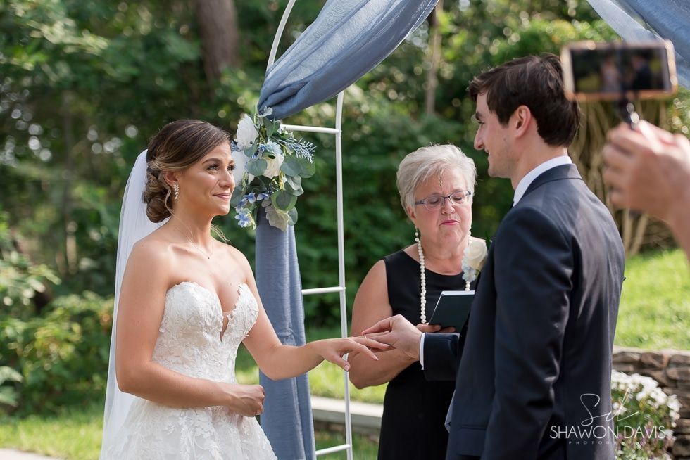 Bride and groom exchange vows under a blue canopy during an outdoor wedding ceremony.