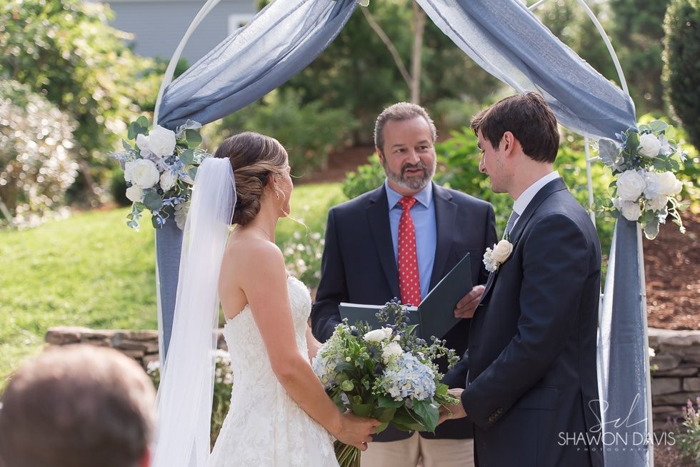 Outdoor wedding ceremony with bride and groom exchanging vows under a floral arch