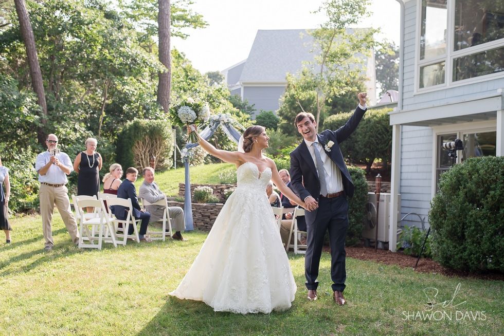 Wedding couple posing outdoors in a garden, smiling with guests seated behind them