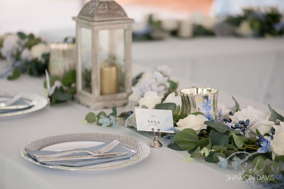 Elegant wedding table centerpiece with lantern, white flowers, greenery, candles, and place settings