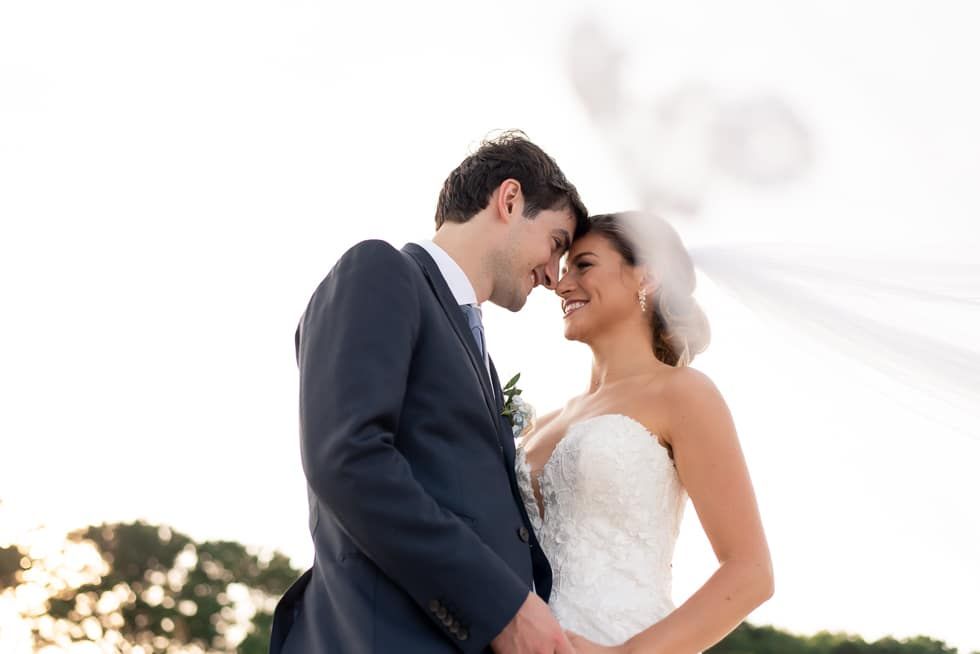 Bride and groom leaning forehead to forehead outdoors, smiling in a wedding portrait
