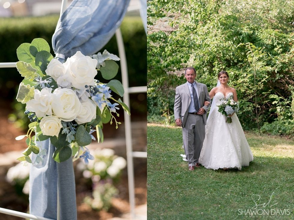Bride and man walking in a garden, with white floral decoration in the foreground.