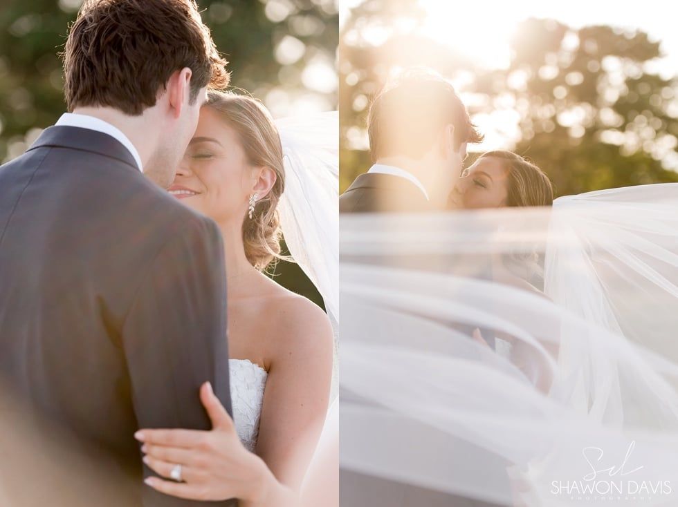 Bride and groom embracing outdoors in soft sunlight, veil flowing in the breeze