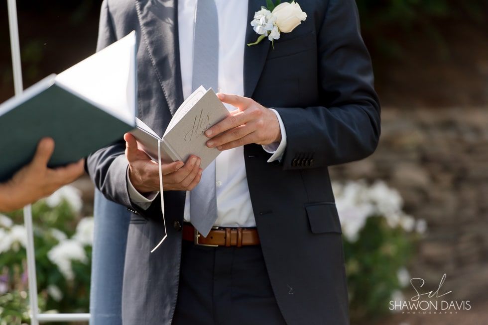 Person in a navy suit holding a book at an outdoor wedding ceremony