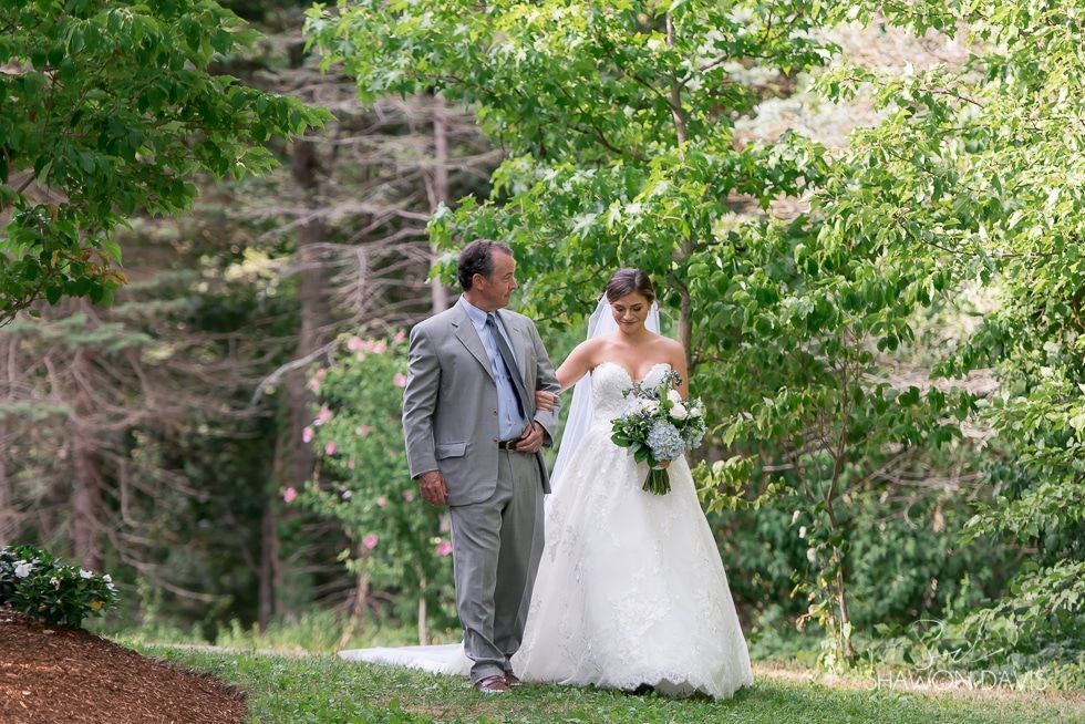 Bride and groom walking together in a green wooded garden, the bride holding a bouquet.
