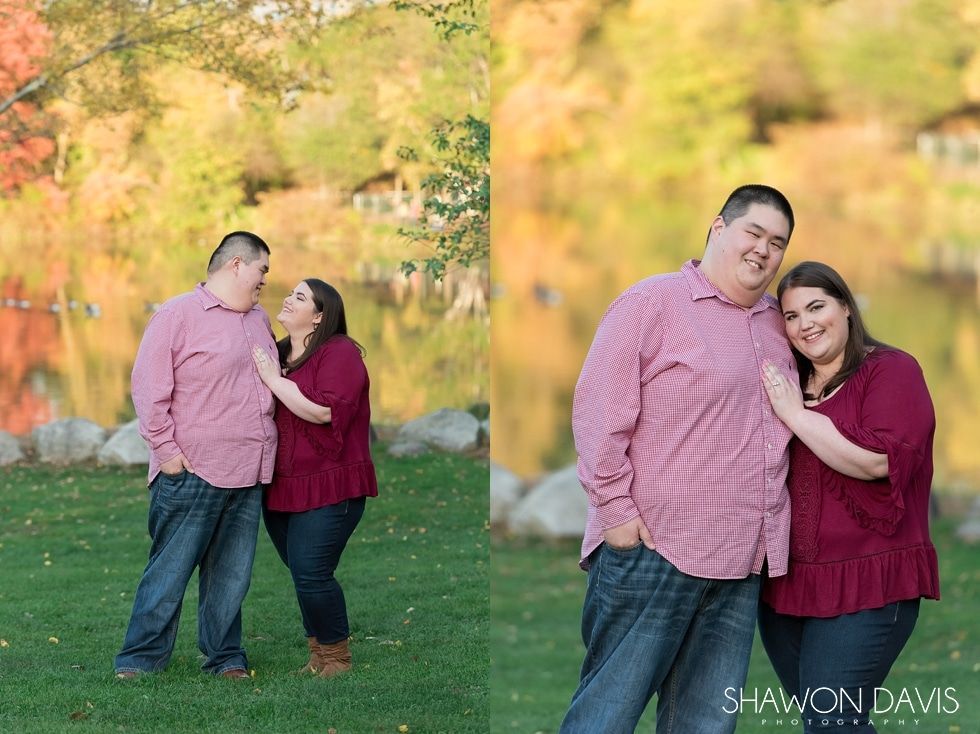Couple in pink tops standing together by a lake with autumn trees reflected in the water